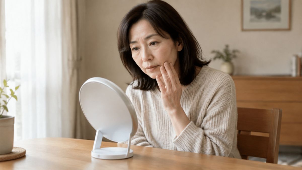 落ち着いた部屋で鏡を見ながら口元や頬のあたりを確認している50代女性の写真